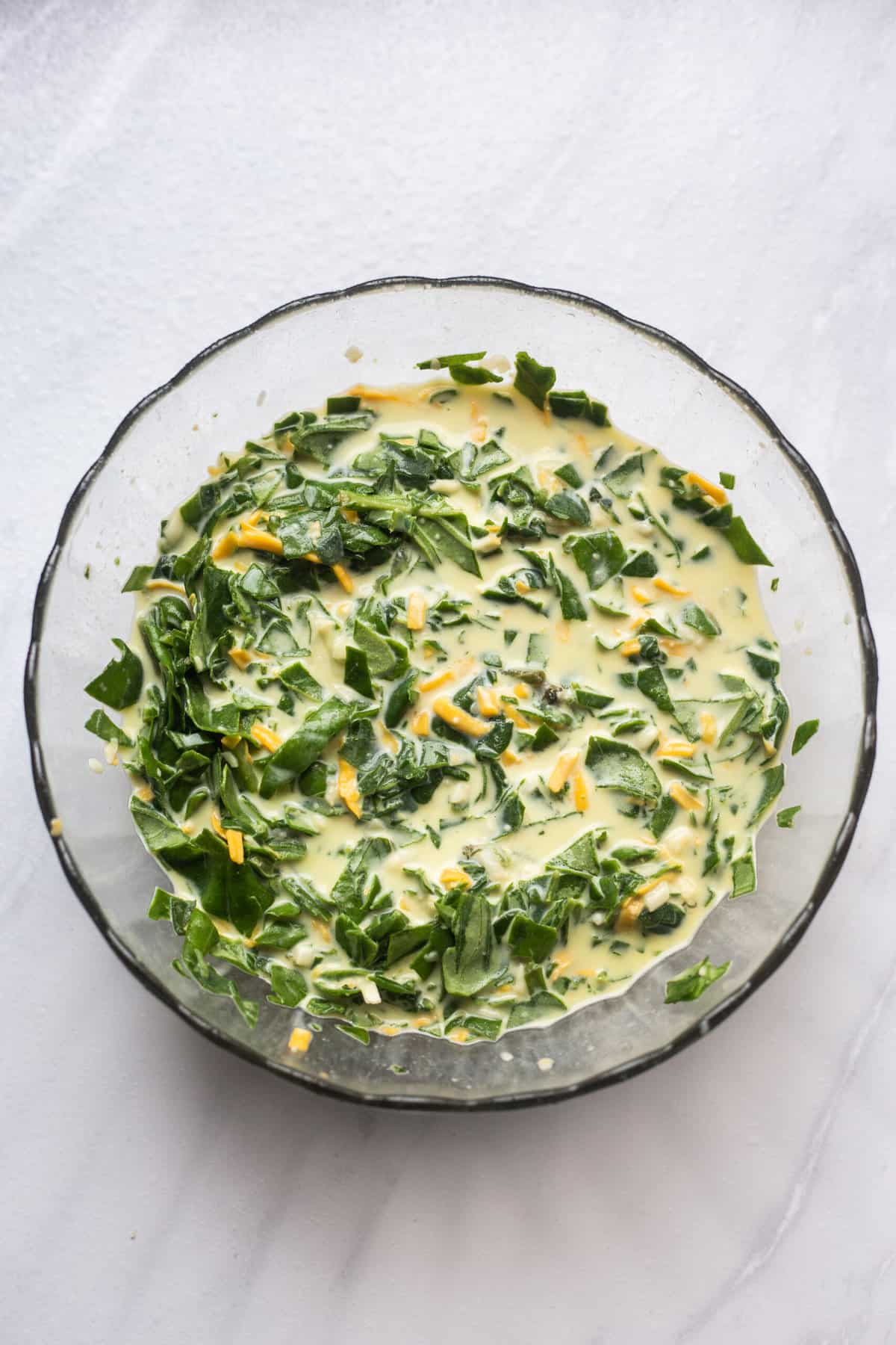 large glass bowl of whole eggs, chopped fresh spinach and shredded cheese