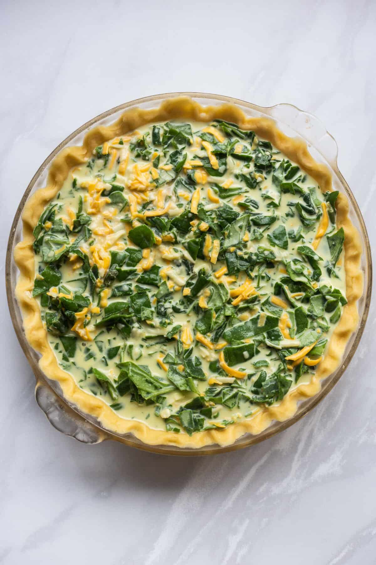 pie dish with unbaked pie crust prepared with the spinach cheese quiche filling