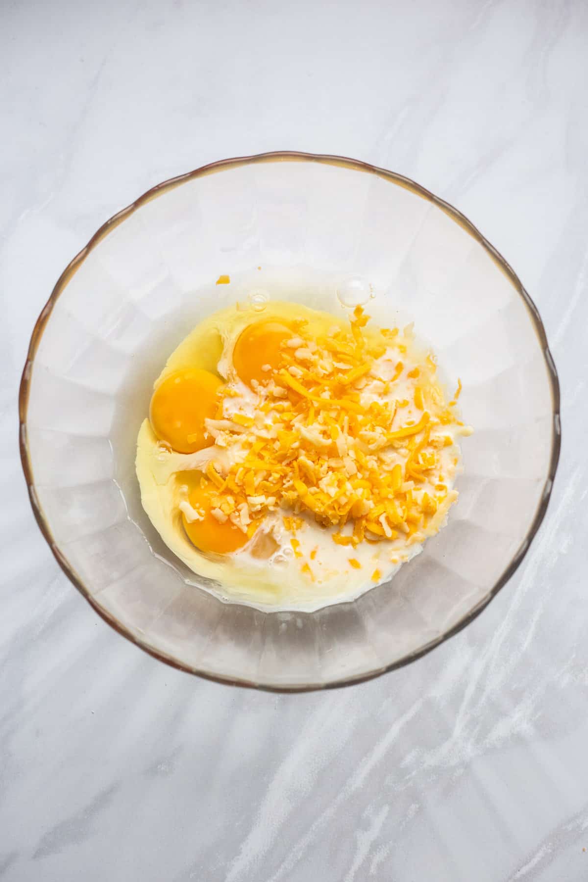large glass bowl of whole eggs and shredded cheese