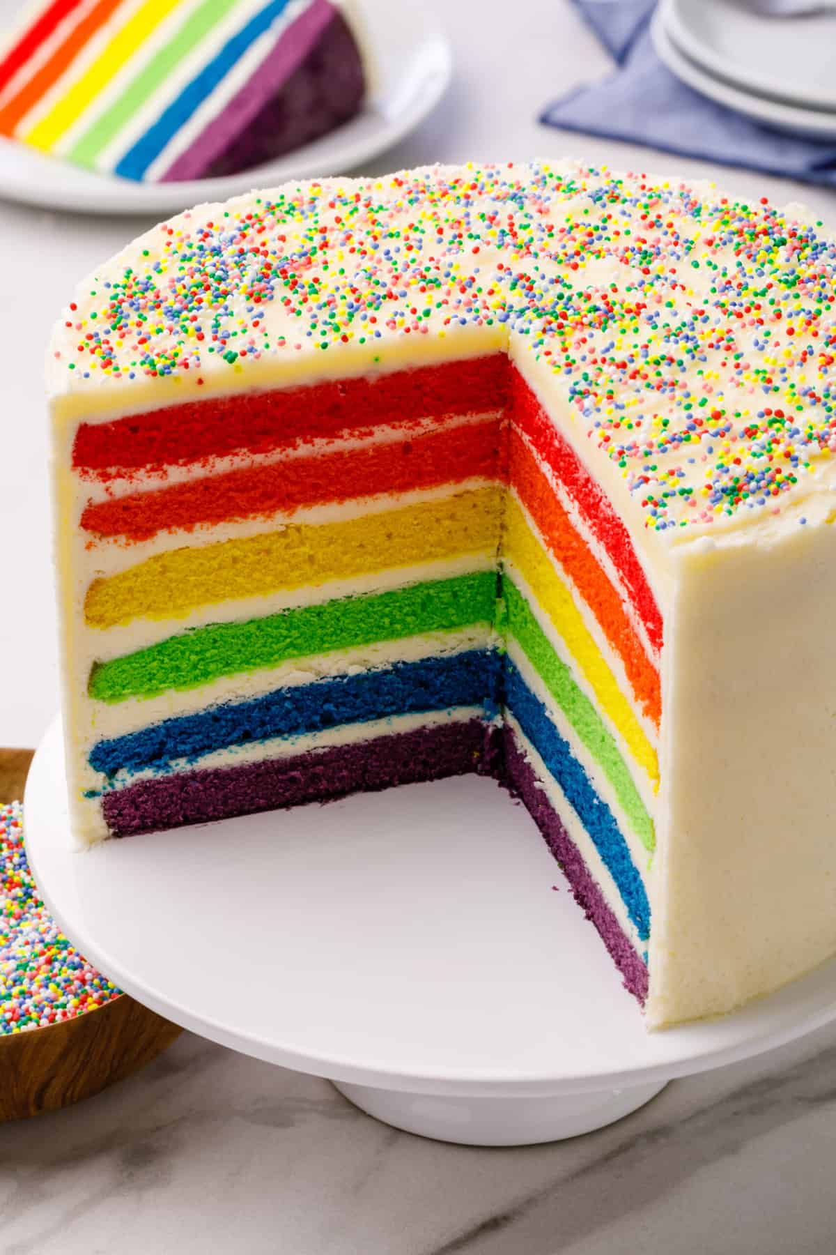 cross section showing rainbow layer cake served on a white cake stand