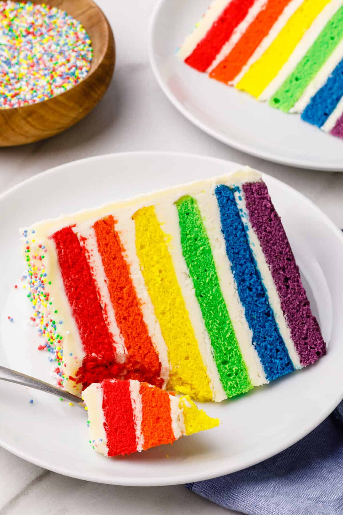 slice of rainbow layer cake served on a white round plate