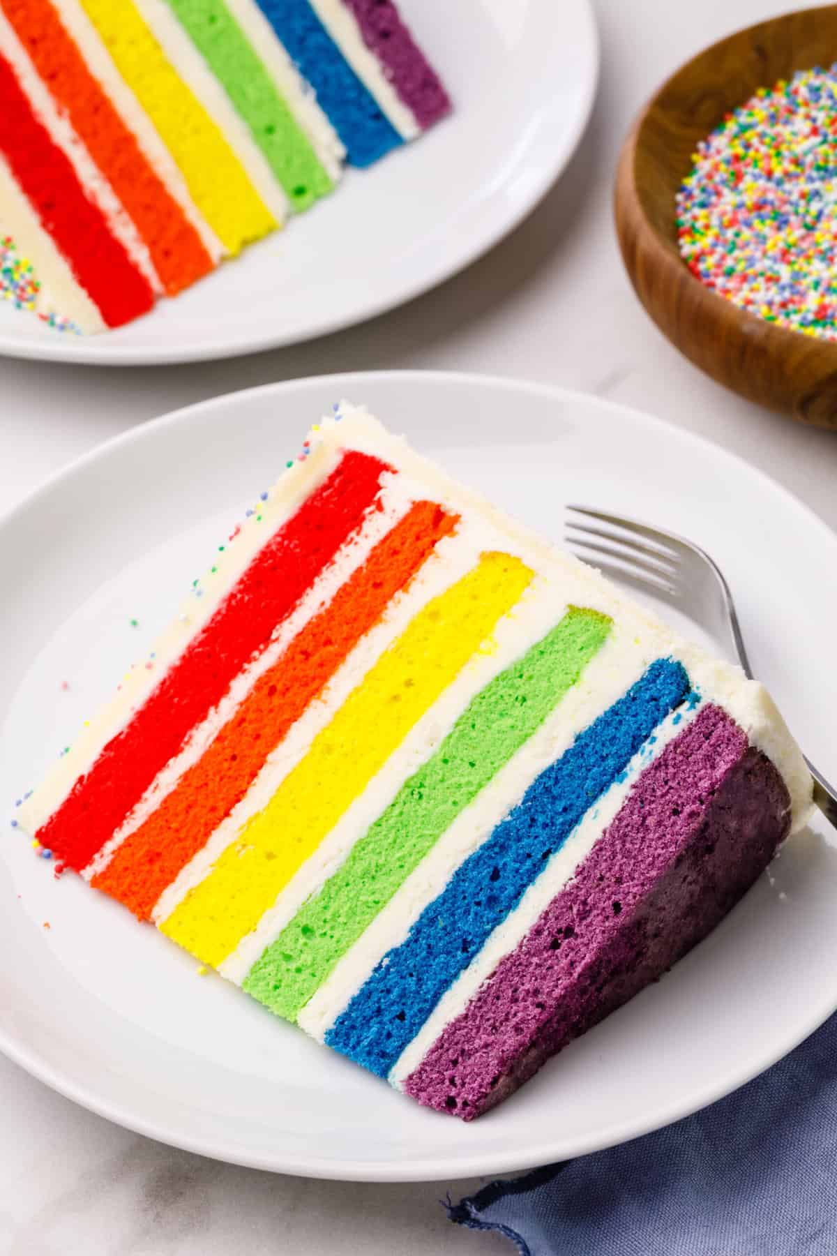 slice of rainbow layer cake served on a white round plate with a silver fork
