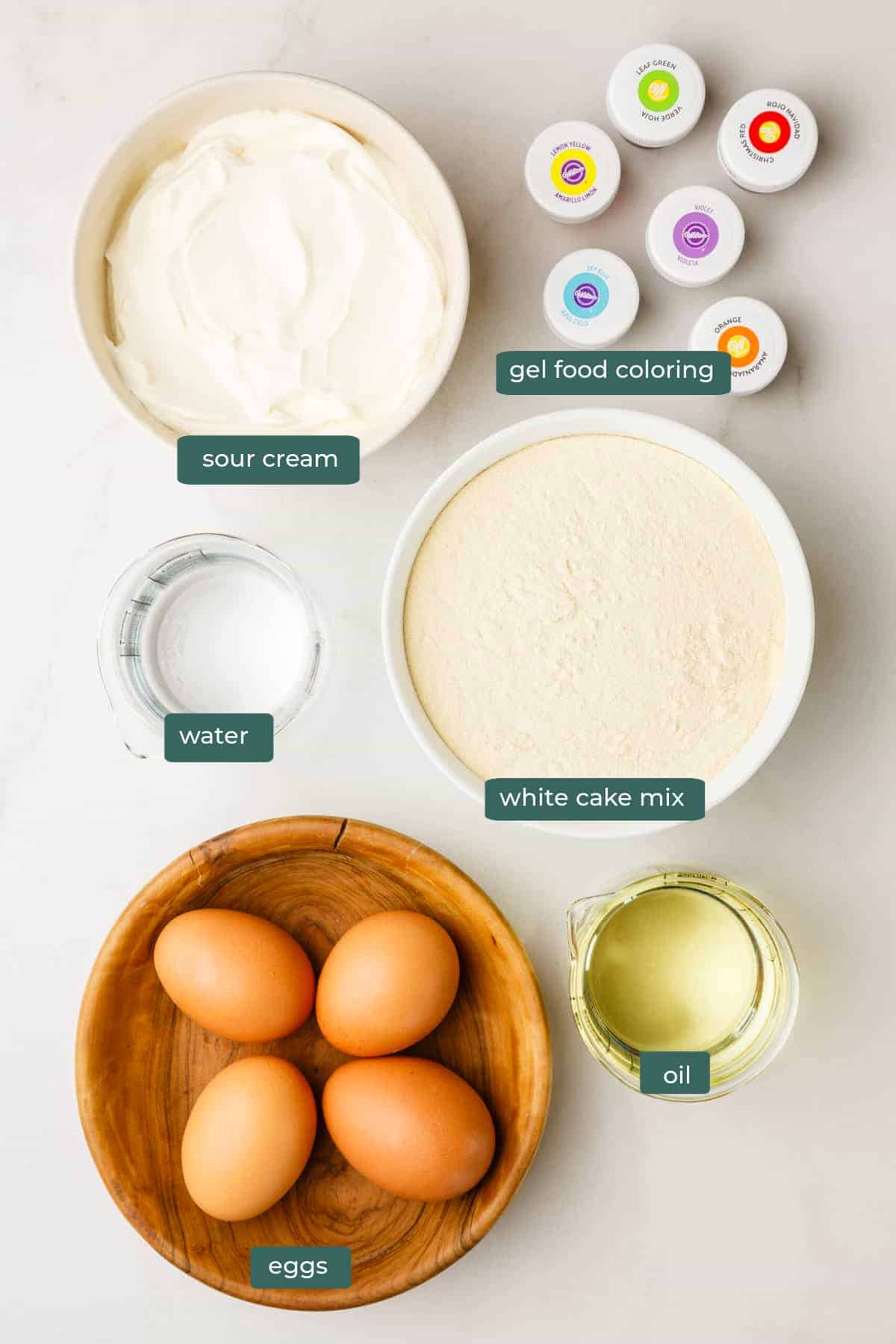 All of the ingredients for rainbow layer cake in bowls on a countertop.