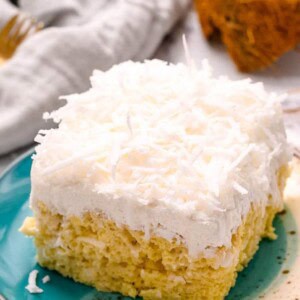A slice of coconut cream cake on a plate with coconut flakes.
