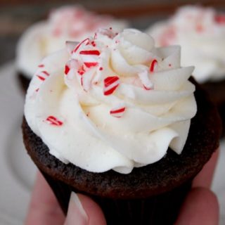 A hand holding a chocolate candy cane cupcake with peppermint butter cream frosting.