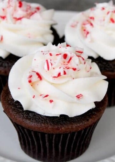 Three chocolate candy cane cupcakes on a plate.