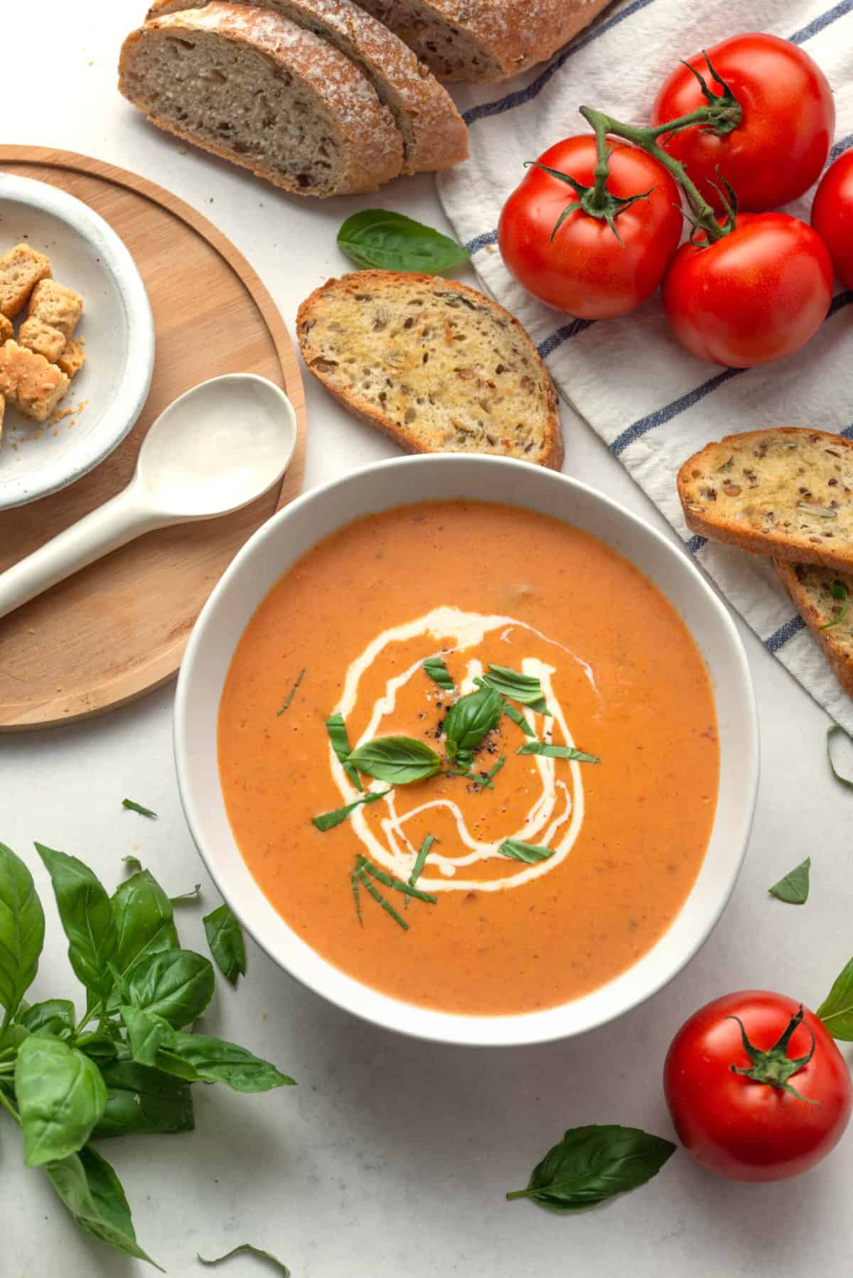 top down image of tomato bisque soup with a swirl of heavy cream and topped with basil