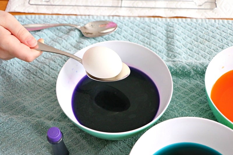 holding the egg on the spoon and getting ready to drop it into the dye 