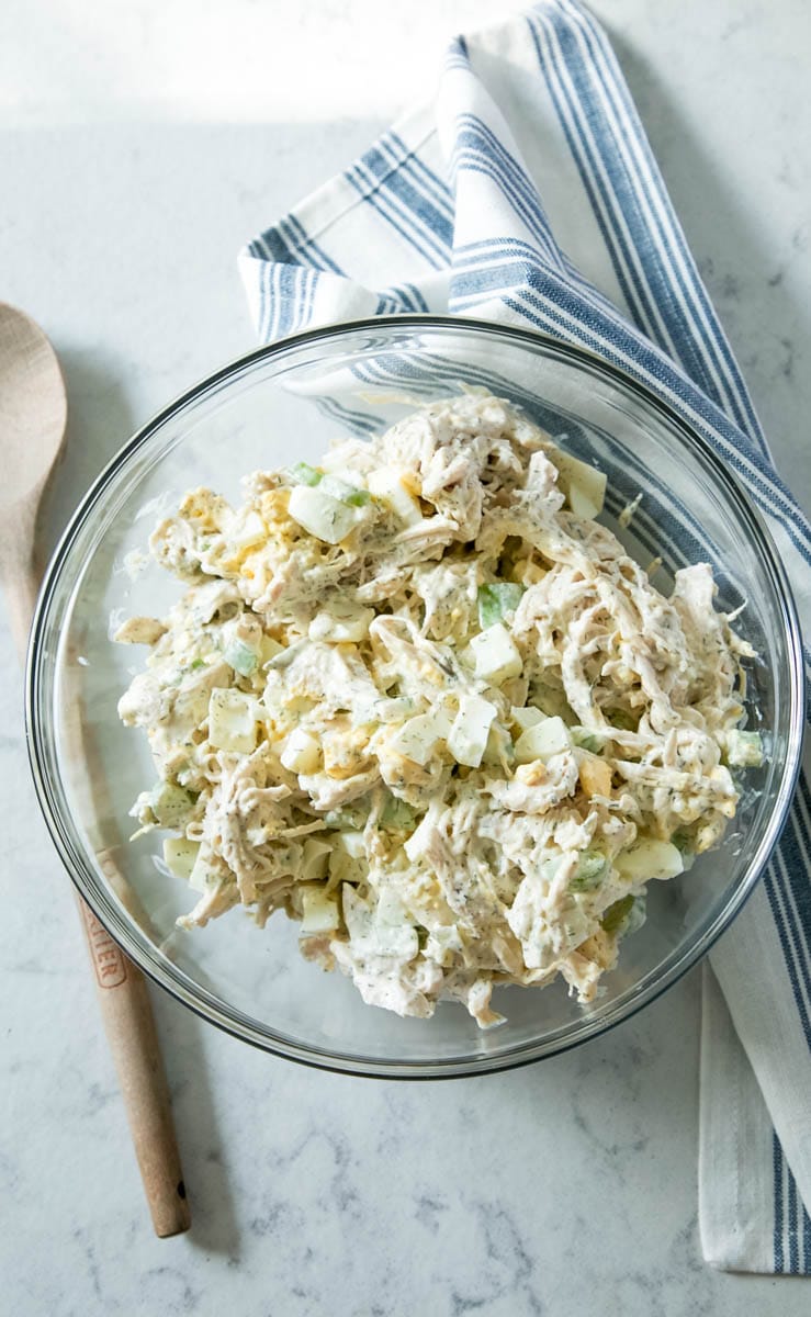 Chicken Salad in a glass bowl with a tea towel and wooden spoon