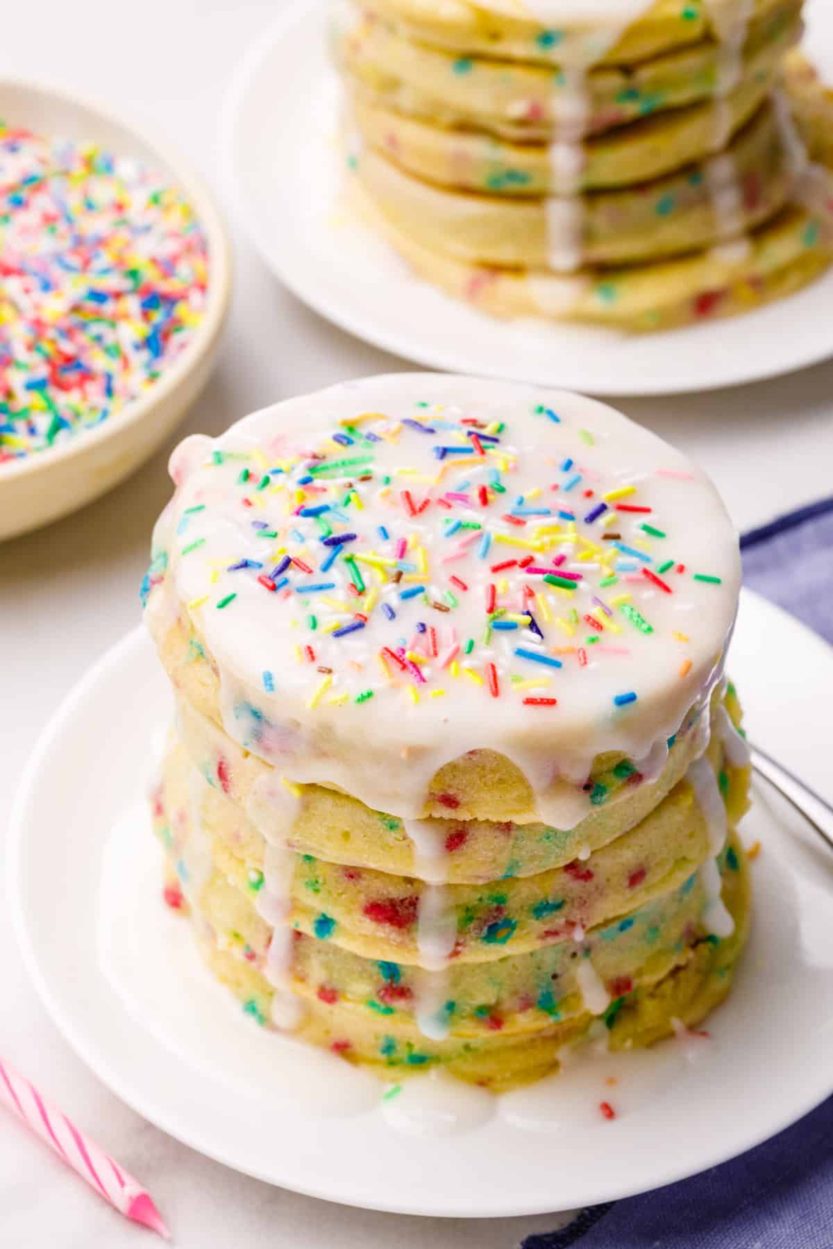 stack of birthday cake pancakes topped with glaze served on white plate