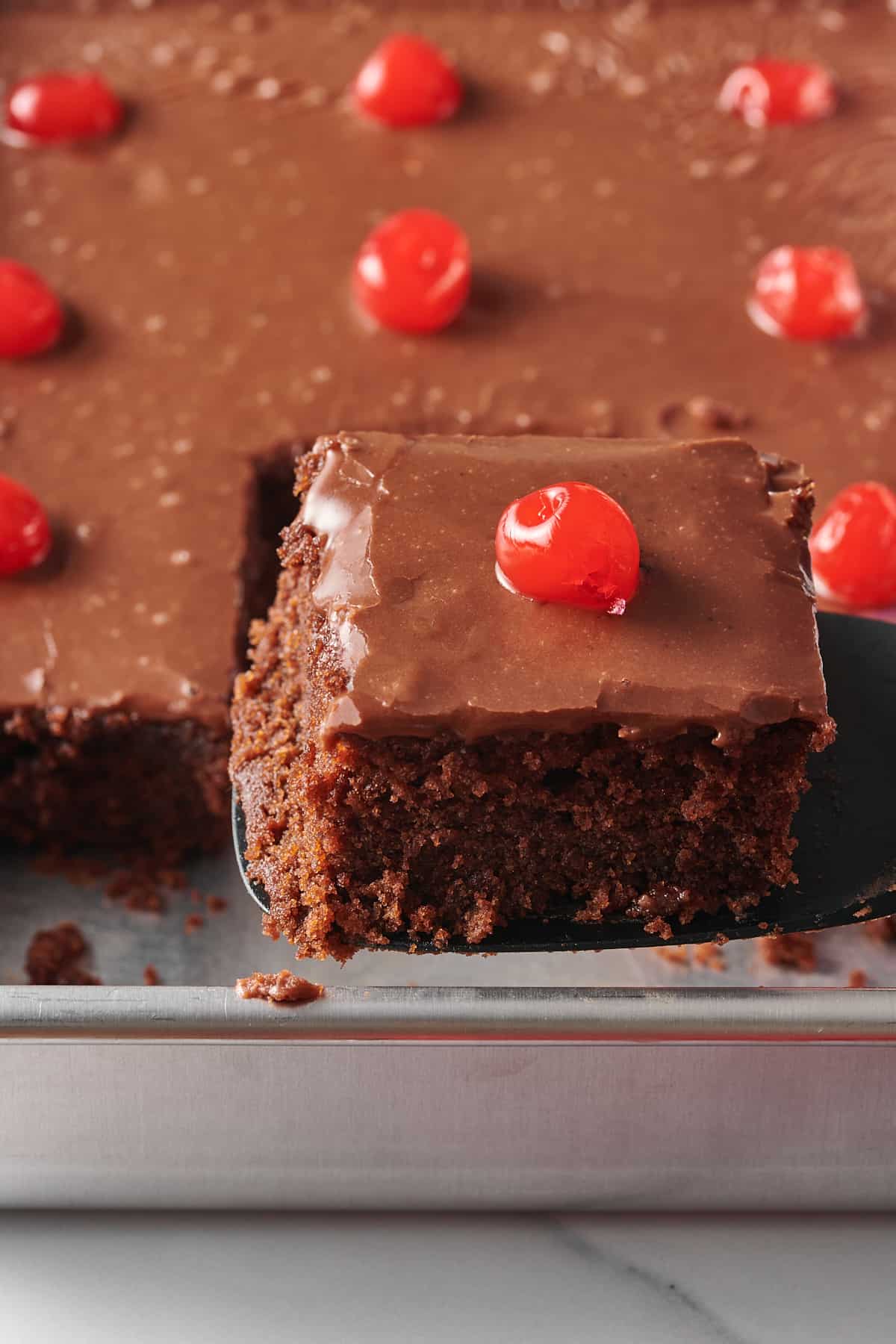 close up image of a square serving of dr pepper cherry cola cake sitting on a metal cake spatula