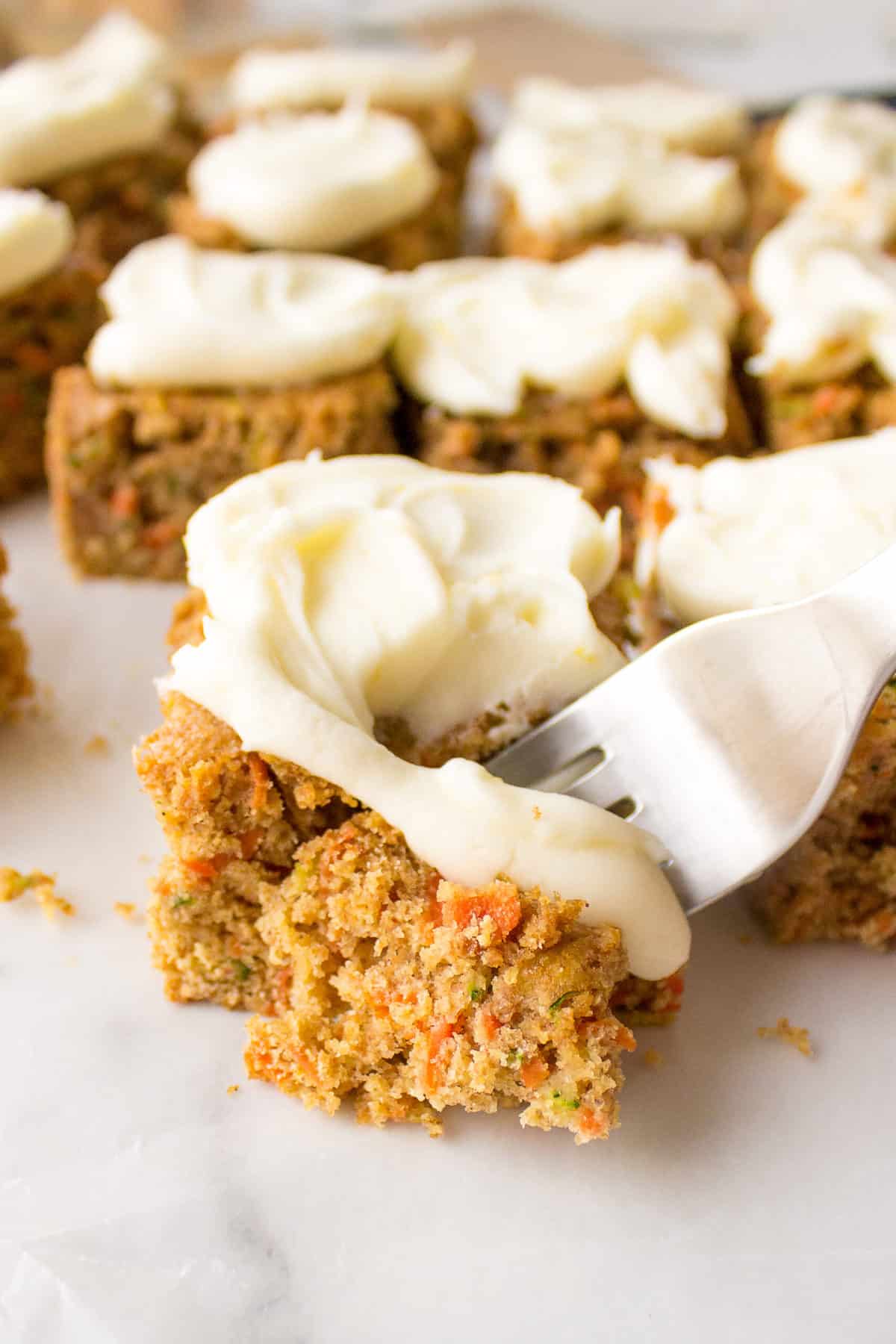 fork digging into homemade zucchini. carrot bars with lemon cream cheese frosting