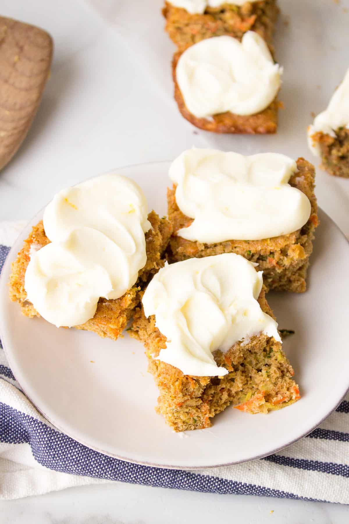 three square slices of zucchini carrot bars with lemon cream cheese frosting served on a round plate