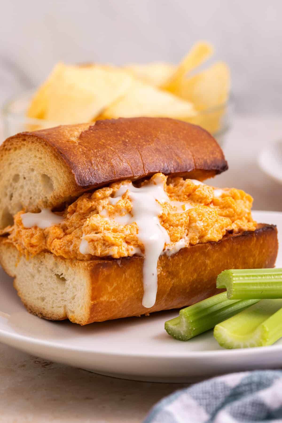 Buffalo chicken sandwich on plate with blue cheese dressing dripping down side.