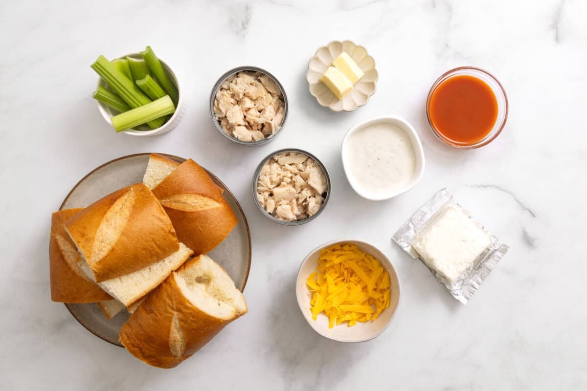 Ingredients for buffalo chicken sandwiches, including canned chicken, cream cheese, cheddar, hot sauce, bread, butter, blue cheese dressing, celery.