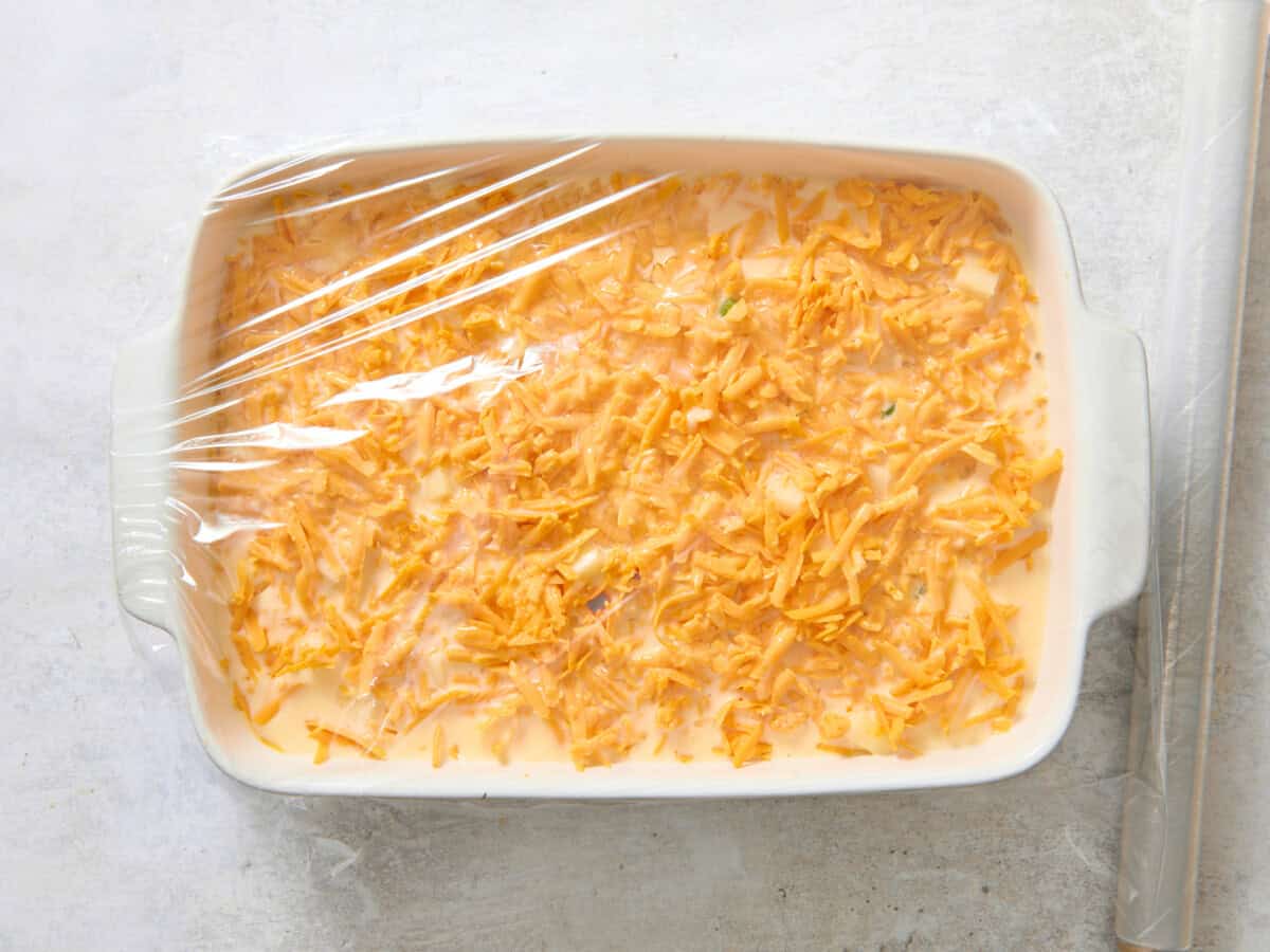 Unbaked overnight breakfast casserole with plastic wrap on top.