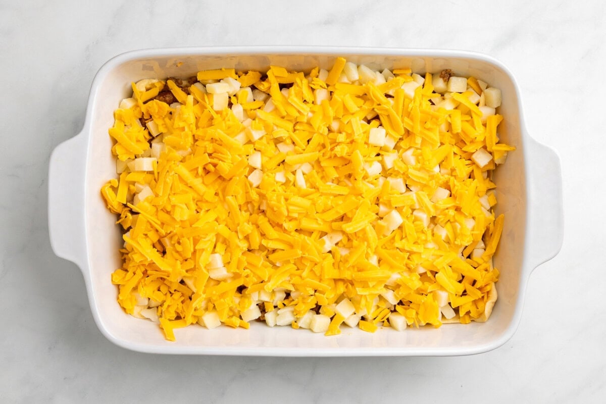 Sausage, cheese, and potatoes layered over crescent roll dough in casserole dish.