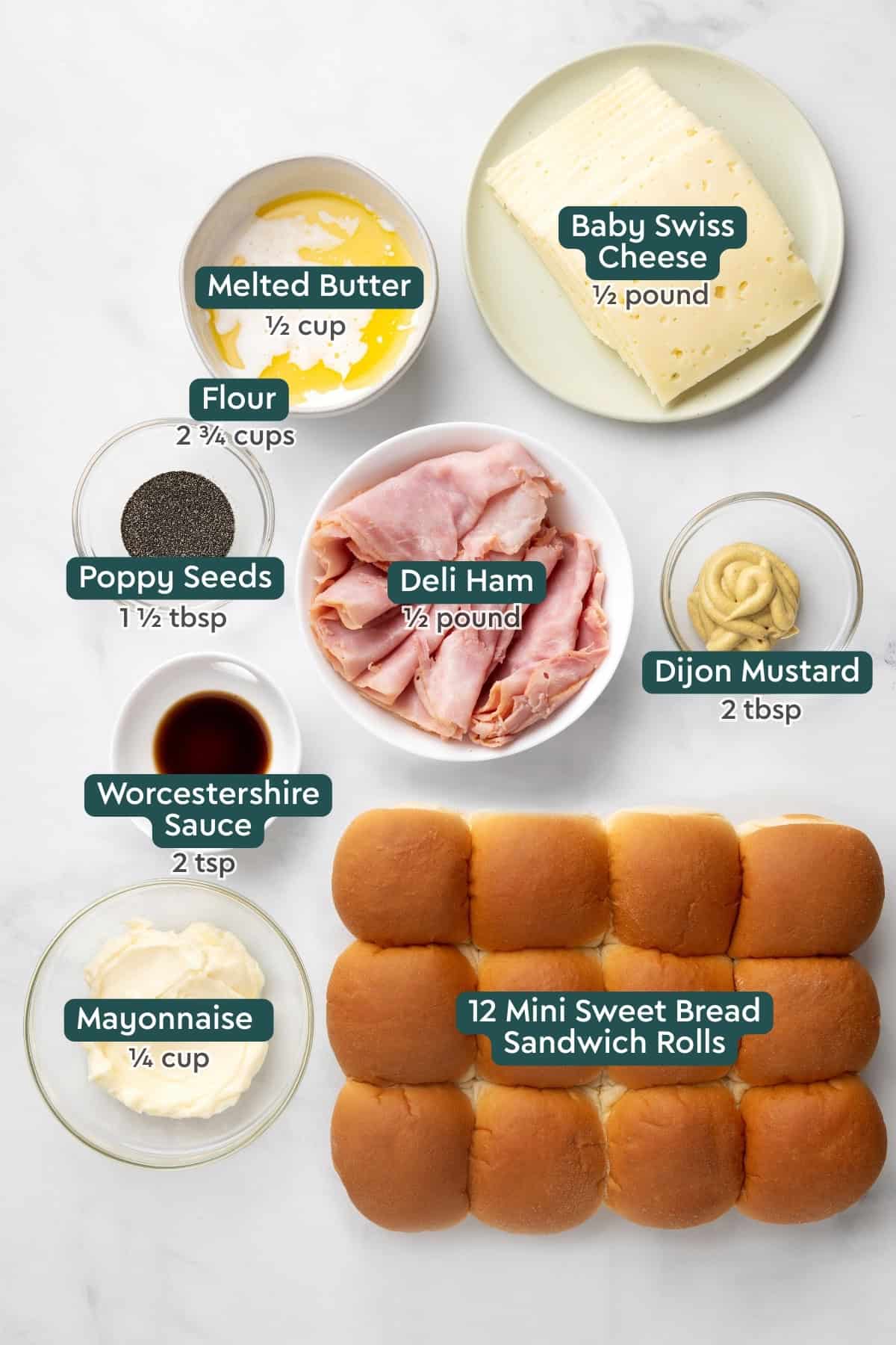 All of the ingredients for ham and swiss sliders in bowls on a white countertop.