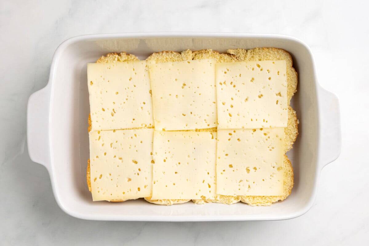 Swiss cheese added to slider rolls in baking dish.