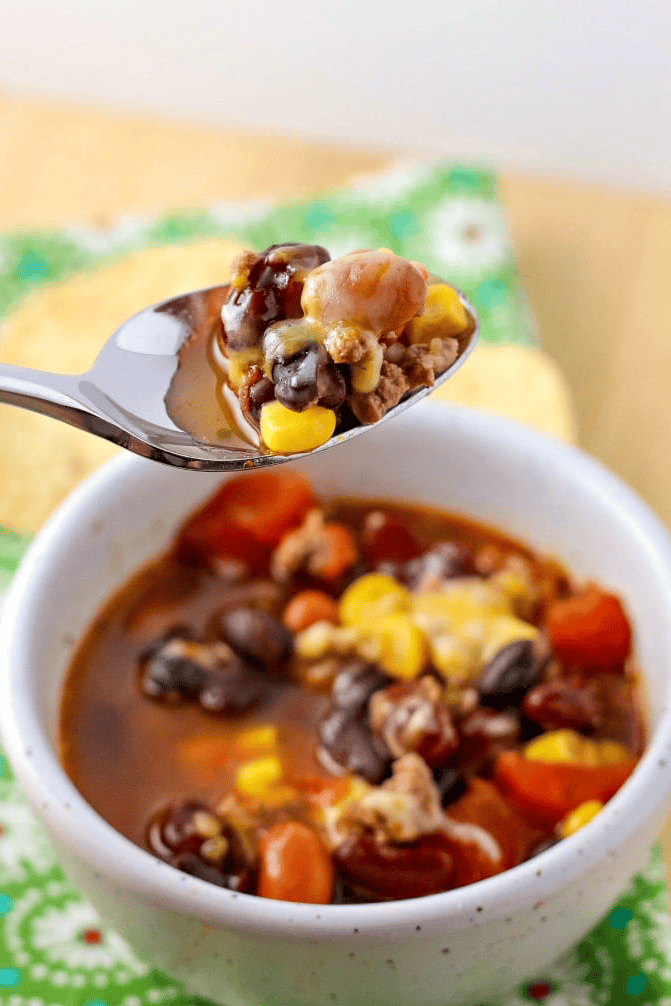 taco soup topped with melted cheese in a white bowl on a table