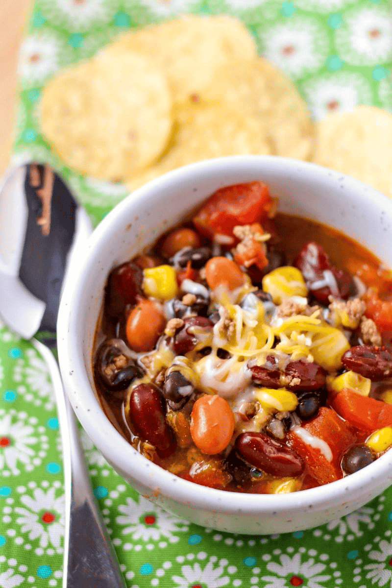 taco soup topped with melted cheese in a white bowl on a table