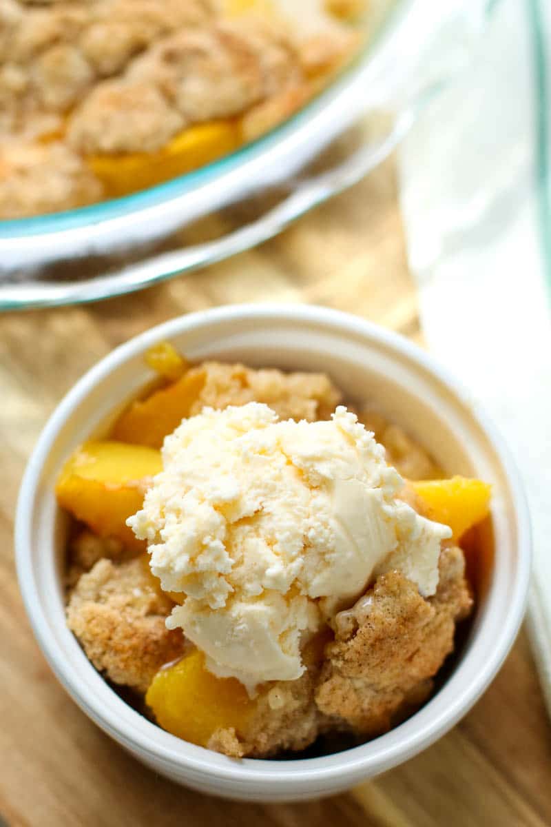 peach cobbler in a bowl topped with vanilla ice cream 