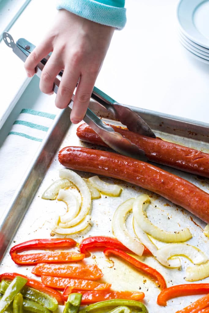 Lifting smoked sausage from sheet pan with tongs.
