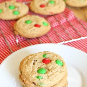 A plate of Christmas M&M cookies and cookies cooling on a wire rack.