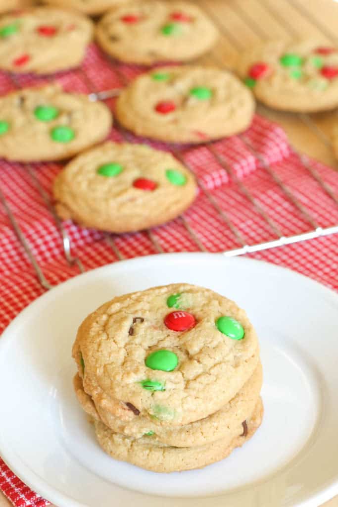 A plate of Christmas M&M cookies and cookies cooling on a wire rack.