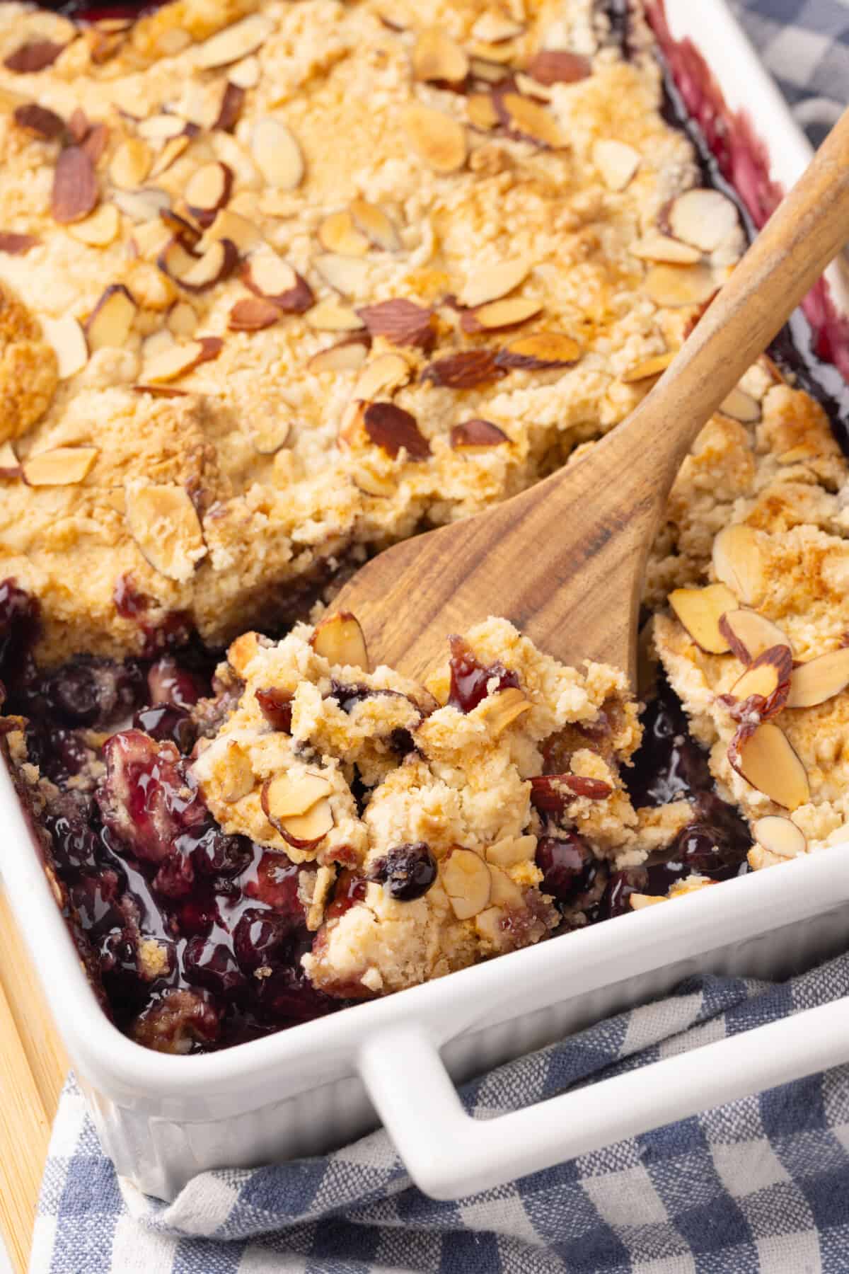 Wooden spoon digging into pan of blueberry dump cake.