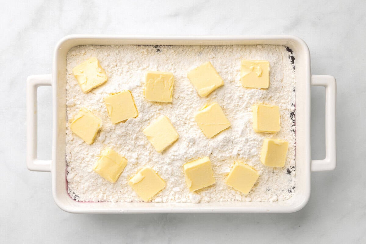 Pats of butter added over cake mix in baking dish.