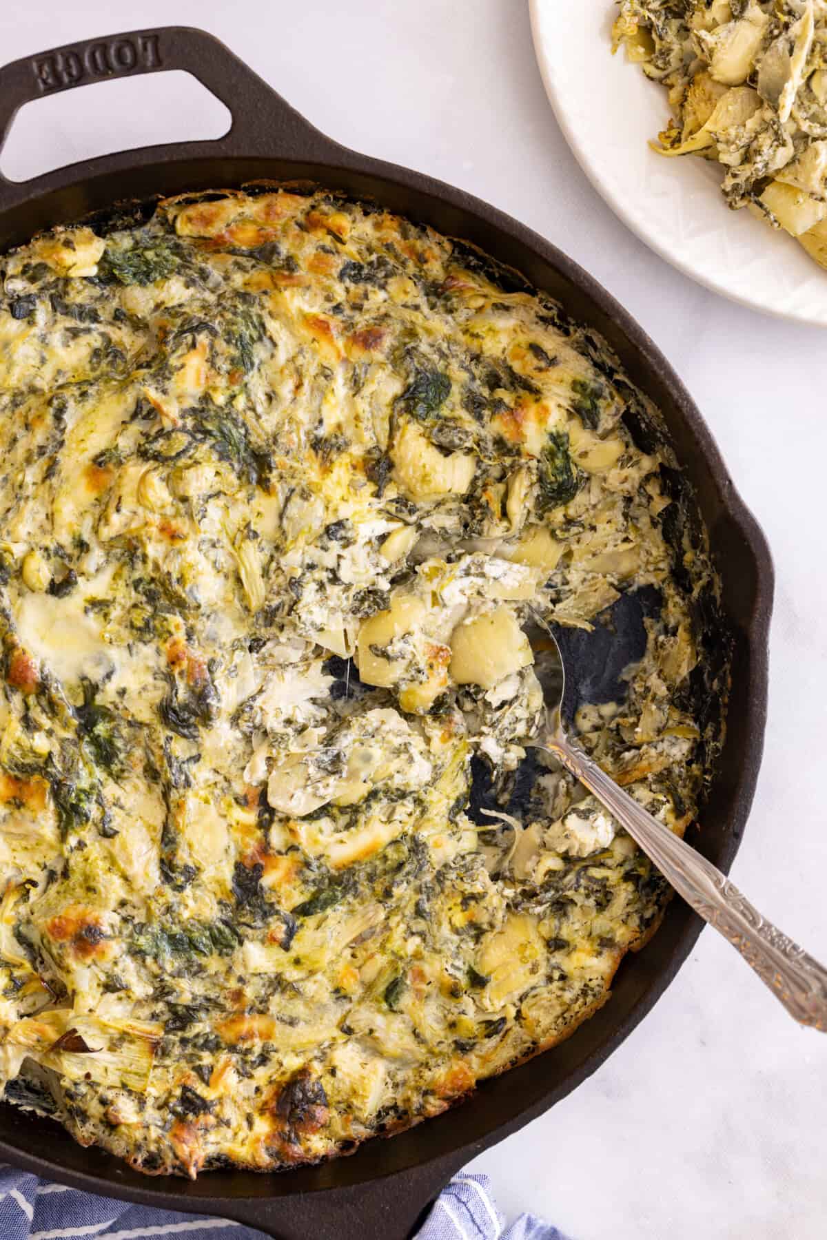 Spoon in cast iron skillet of spinach artichoke dip.