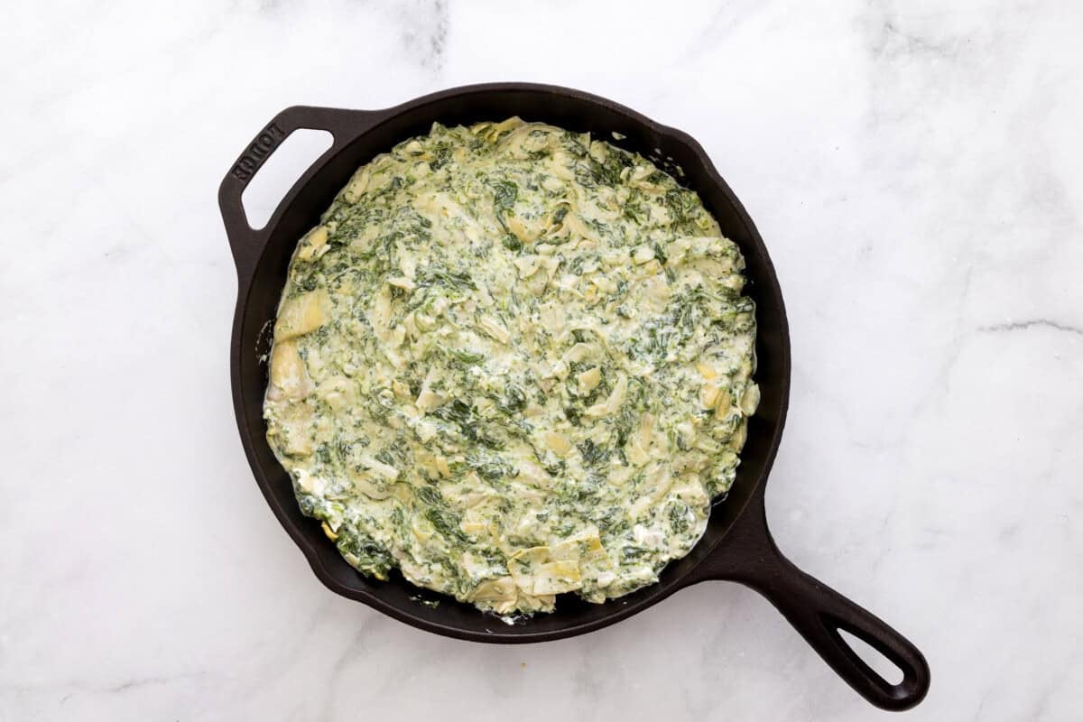 Spinach artichoke dip spread into cast iron skillet.