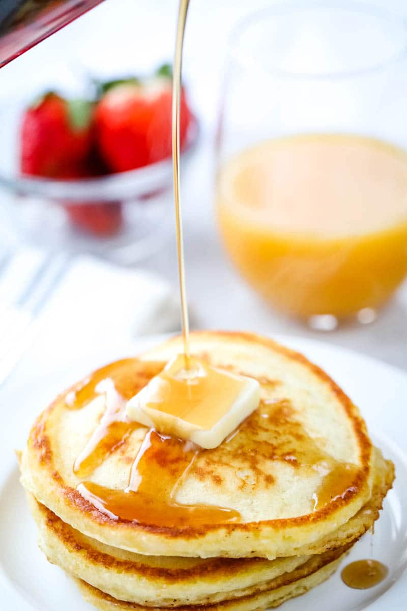 fluffy pancakes with butter on top being coated with syrup