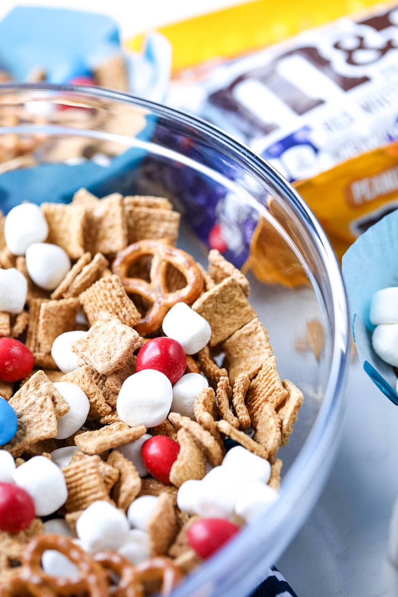 A bowl of snack mix with m&ms, chex mix, pretzels, and marshmallows.