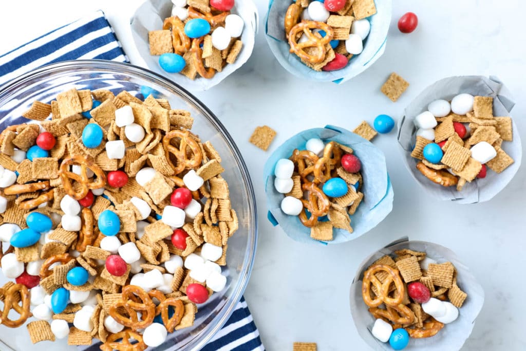 An overhead view of a bowl of snack mix and cups of snack mix.