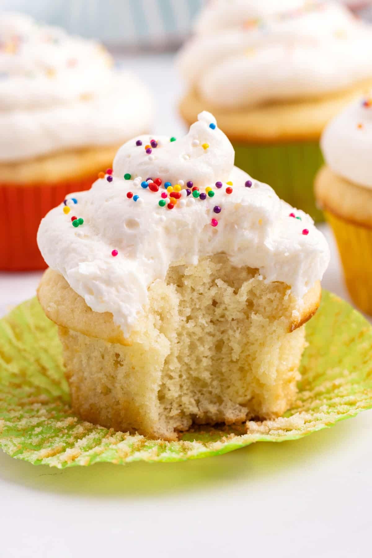 Cupcake topped with fluffy buttercream frosting, with bite taken out.