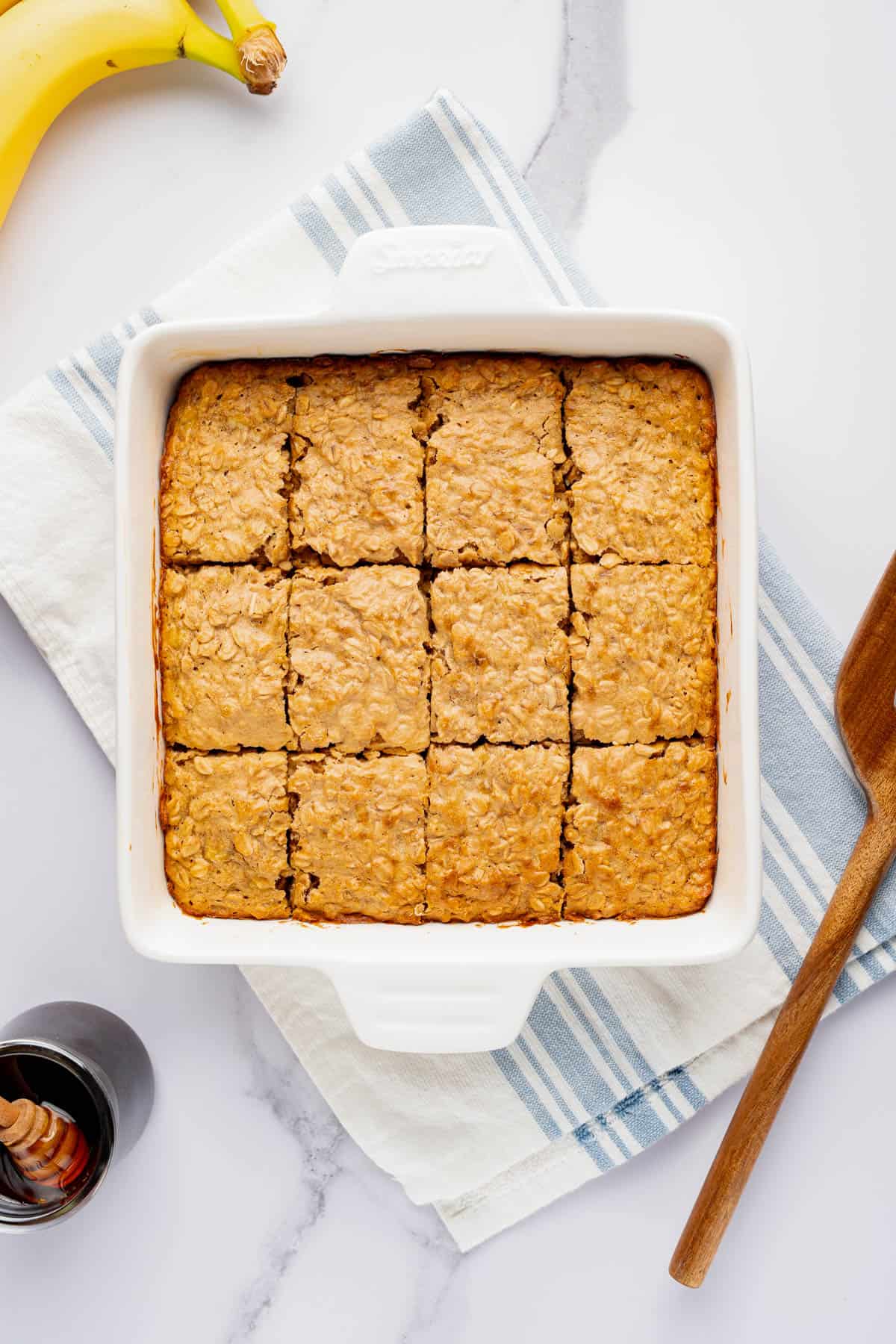 Sliced peanut butter banana oatmeal bars in baking dish set on striped tea towel.