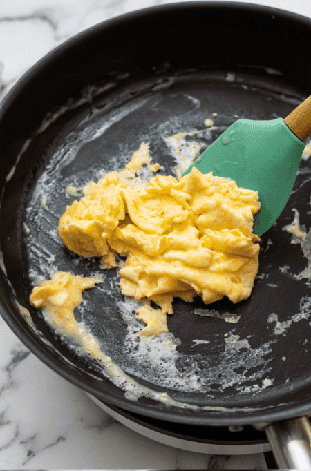 Rubber spatula pushing scrambled eggs in skillet.