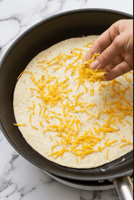 Sprinkling cheese on tortilla in skillet.