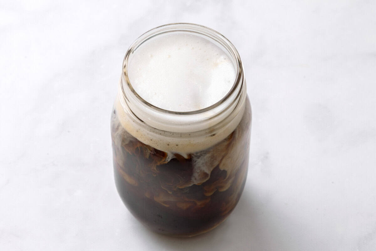 Milk foam added to mason jar with pumpkin spice cold brew coffee.