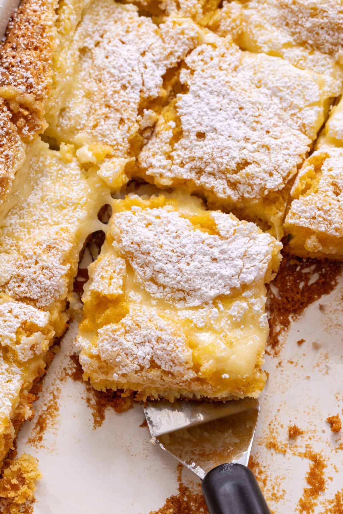 Spatula lifting slice of ooey gooey butter cake from pan.