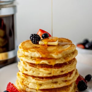 A stack of homemade buttermilk pancakes topped with berries, butter, and syrup.
