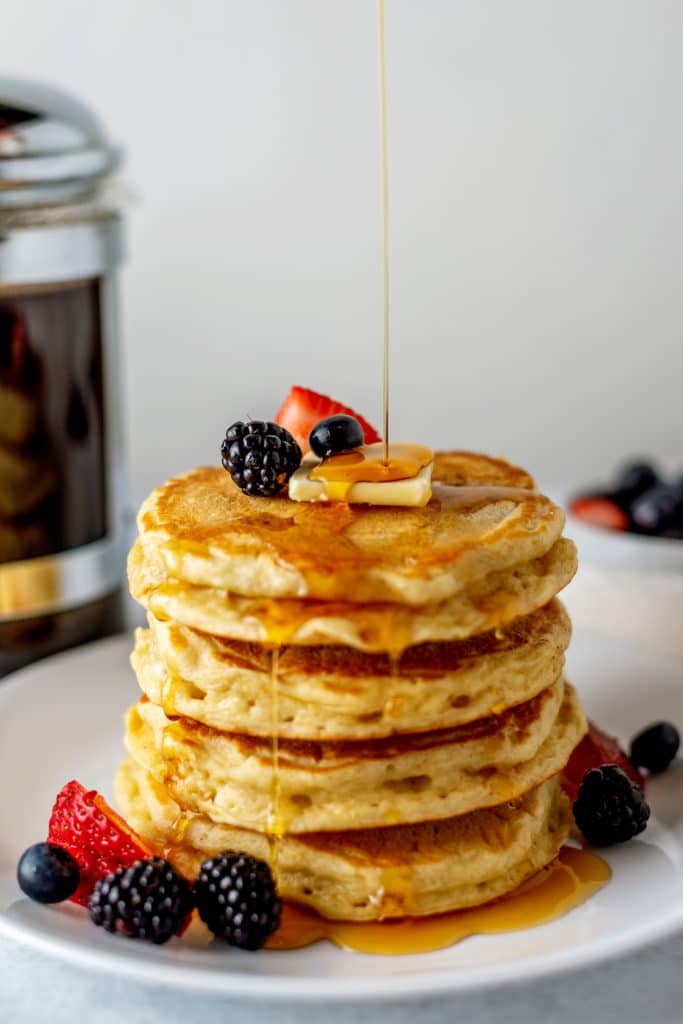A stack of homemade buttermilk pancakes topped with berries, butter, and syrup.
