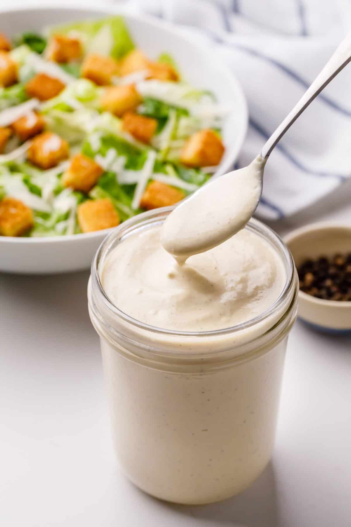 caesar dressing served in a jar with a silver spoon spoonful
