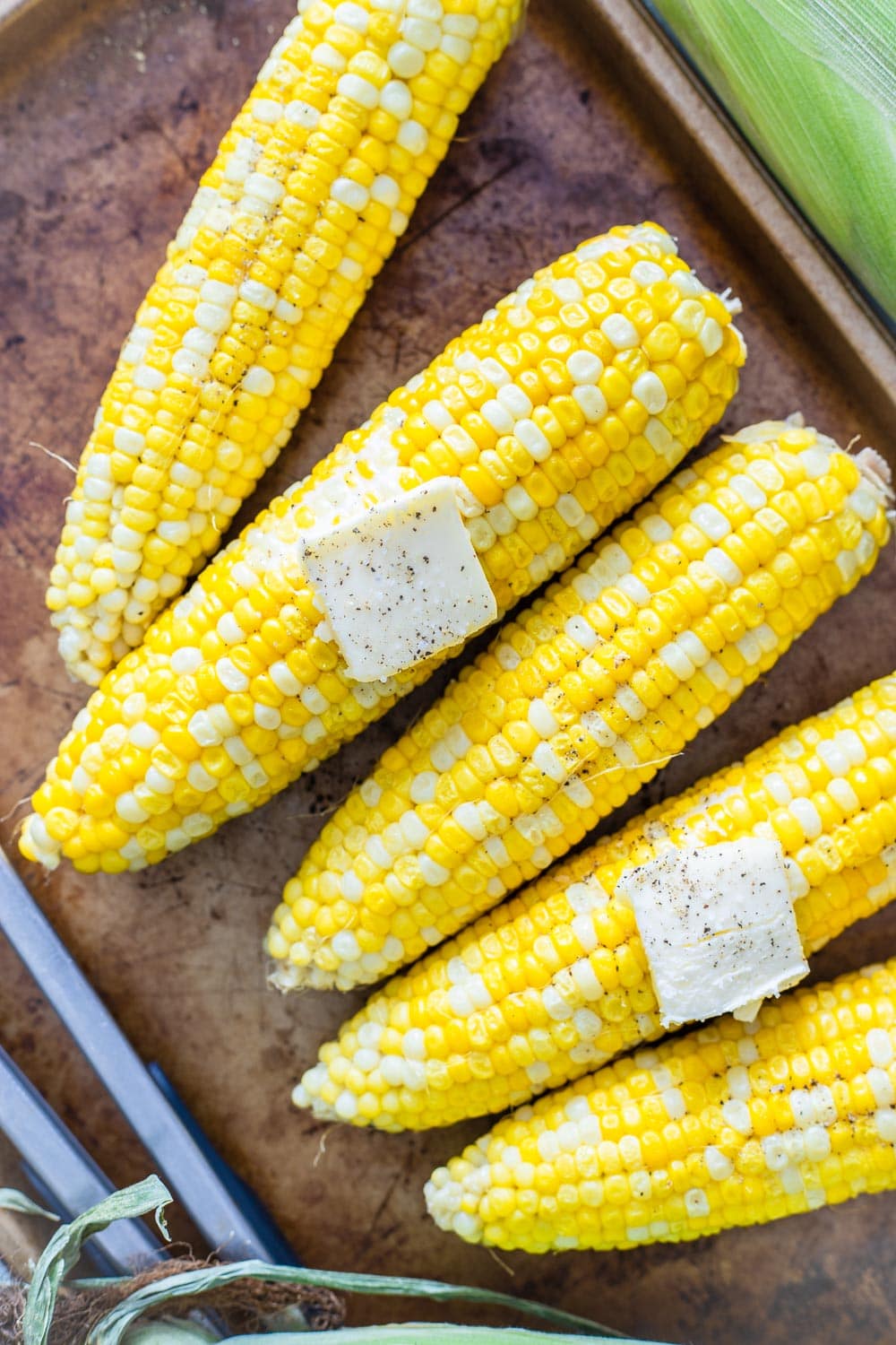 Ears of corn in a row with pats of butter on top. 