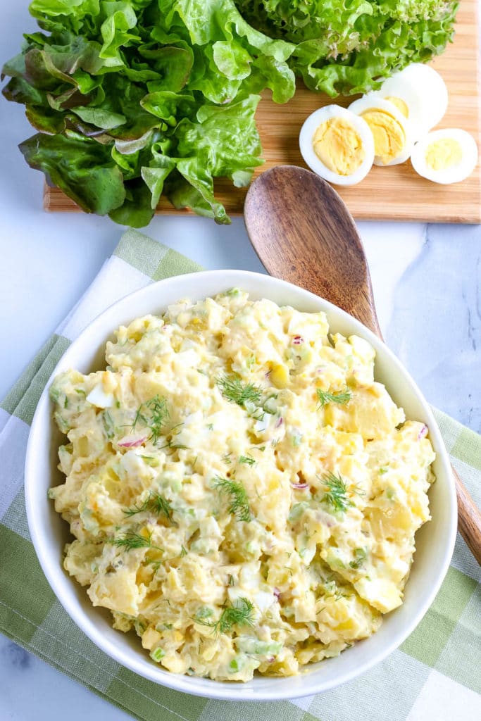 potato salad in a white bowl with a wooden serving spoon 