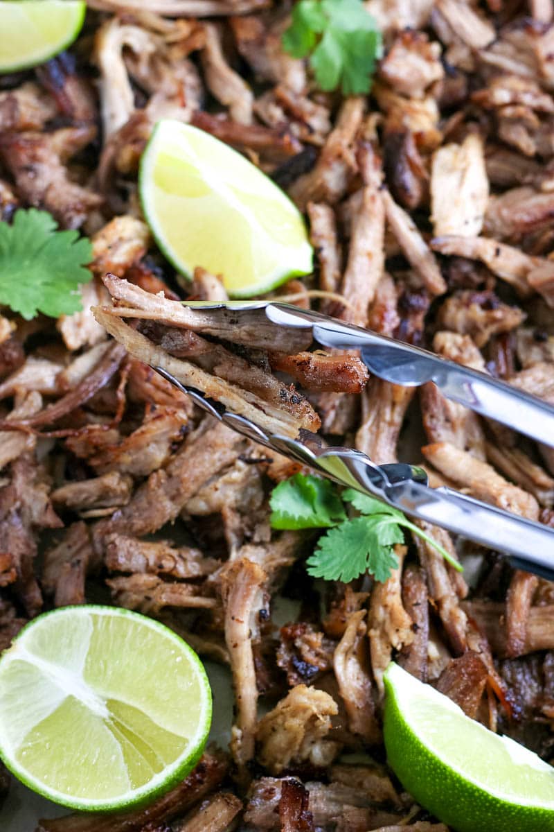 slow cooker pork carnitas with tongs and lime wedges 