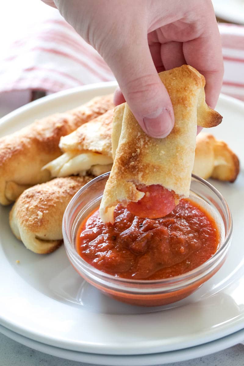 dipping pepperoni sticks into marinara sauce 