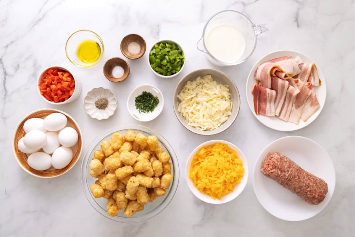Ingredients for tater tot breakfast casserole, including breakfast sausage, bacon, bell peppers, eggs, milk, cheese, frozen tater tots.